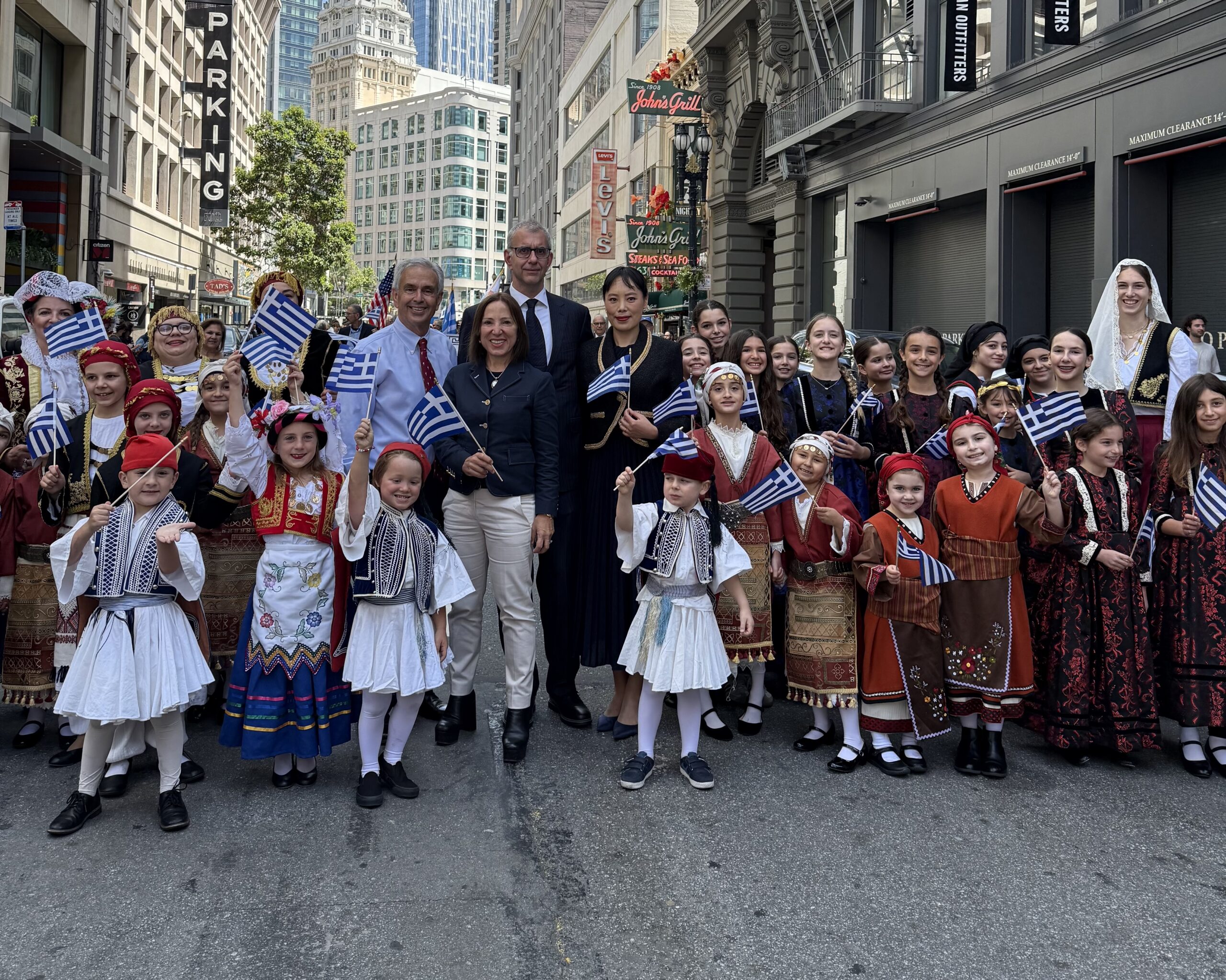 Image of Lt. Gov. Kounalakis with a group of parade goers, many of whom are dressed in Greek clothing and waving Greek flags.