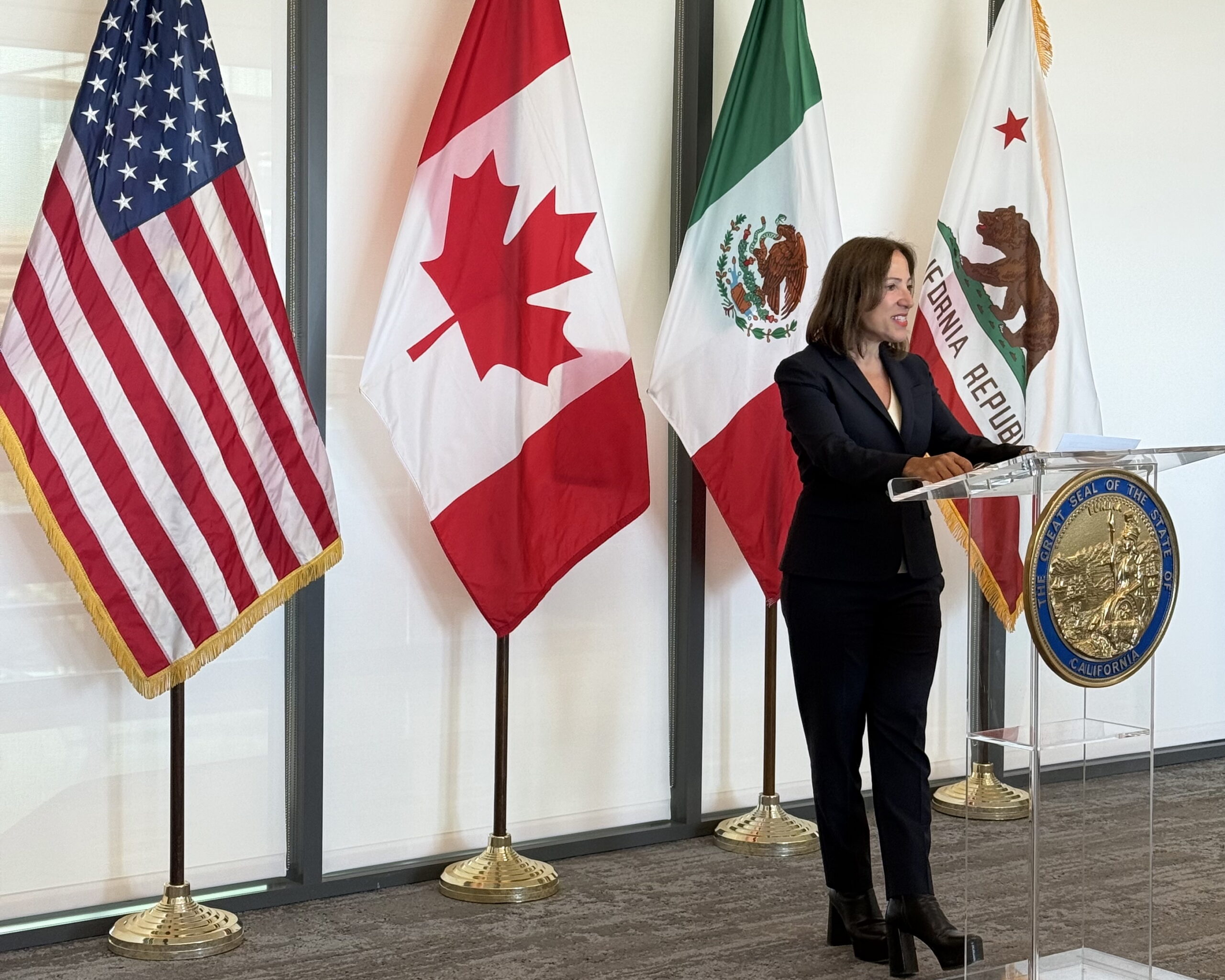 Image of Lt. Gov. Kounalakis at the podium with the the flags of the United States, Canada, Mexico and California